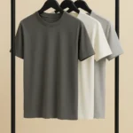 Three premium cotton crew neck t-shirts in charcoal, off-white, and light grey hanging on black hangers.